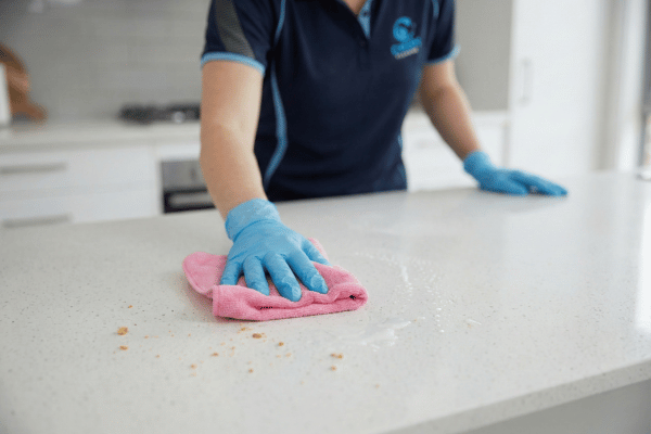 Cleaner wiping and sanitising a granite kitchen benchtop in a residential home.